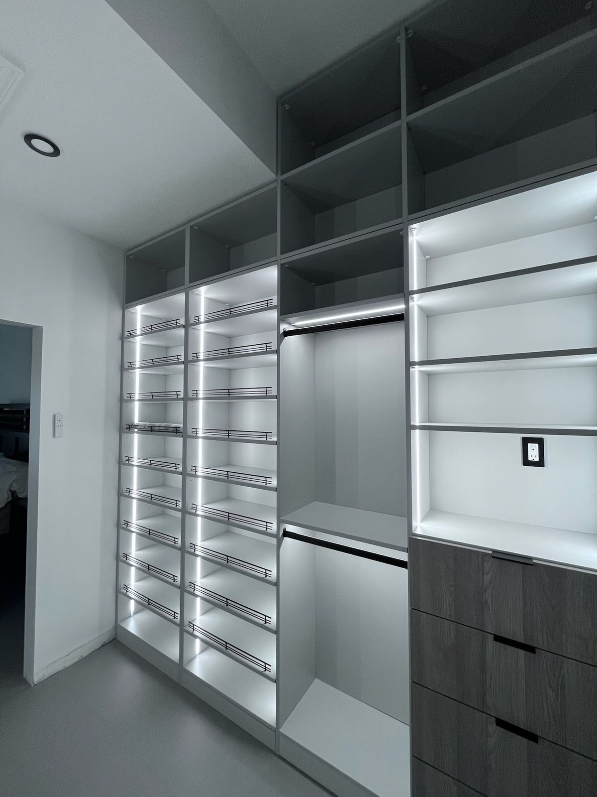 Wall of lit shoe shelves, hanging space and wood drawers